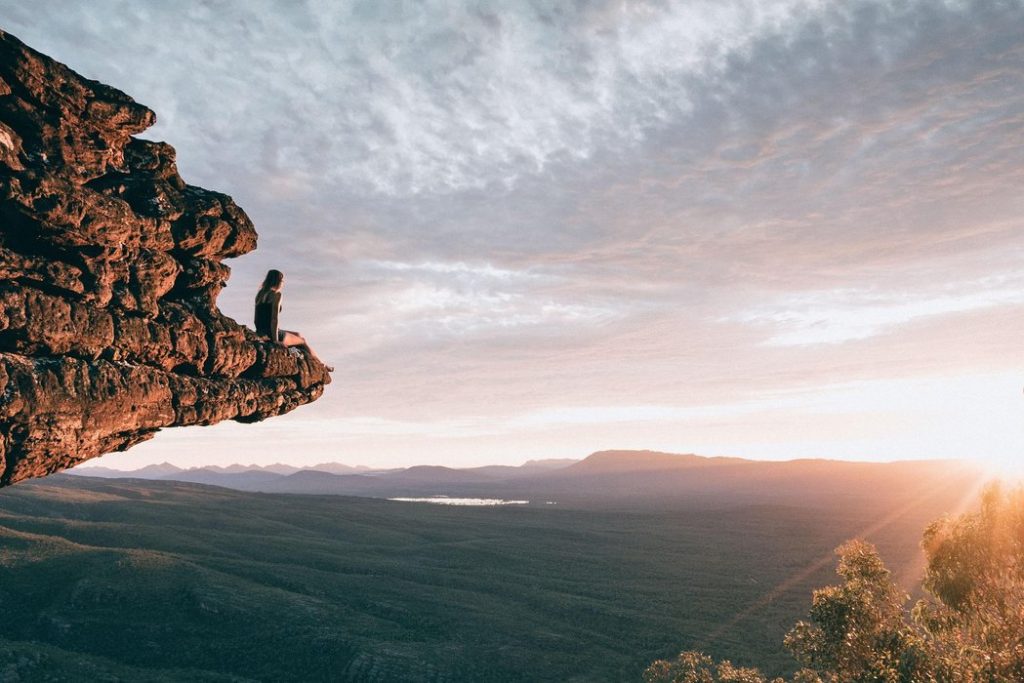 An adventurous woman traveller sitting in the top of the mountain and starring the view