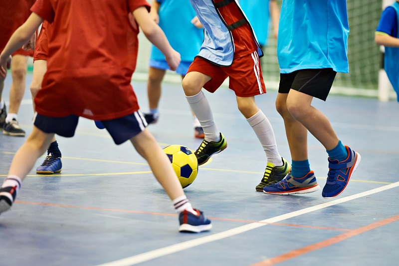 A Group of Kids playing football in an indoor stadium two kids were trying to kick the football.