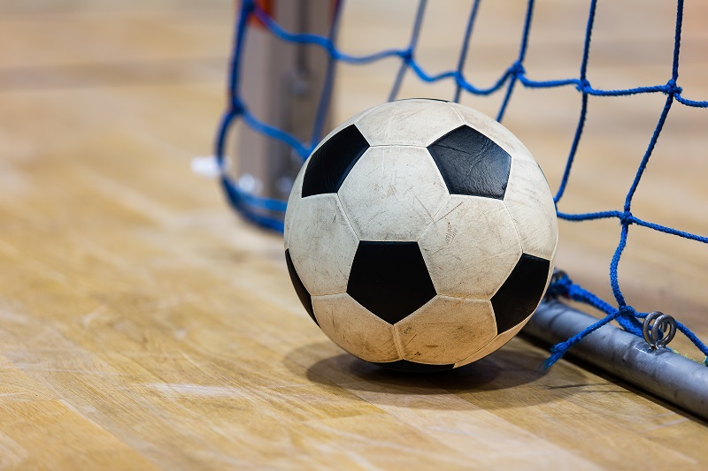 In an indoor soccer stadium the futsal ball it is in black and white colour, the ball reached the goal post.
